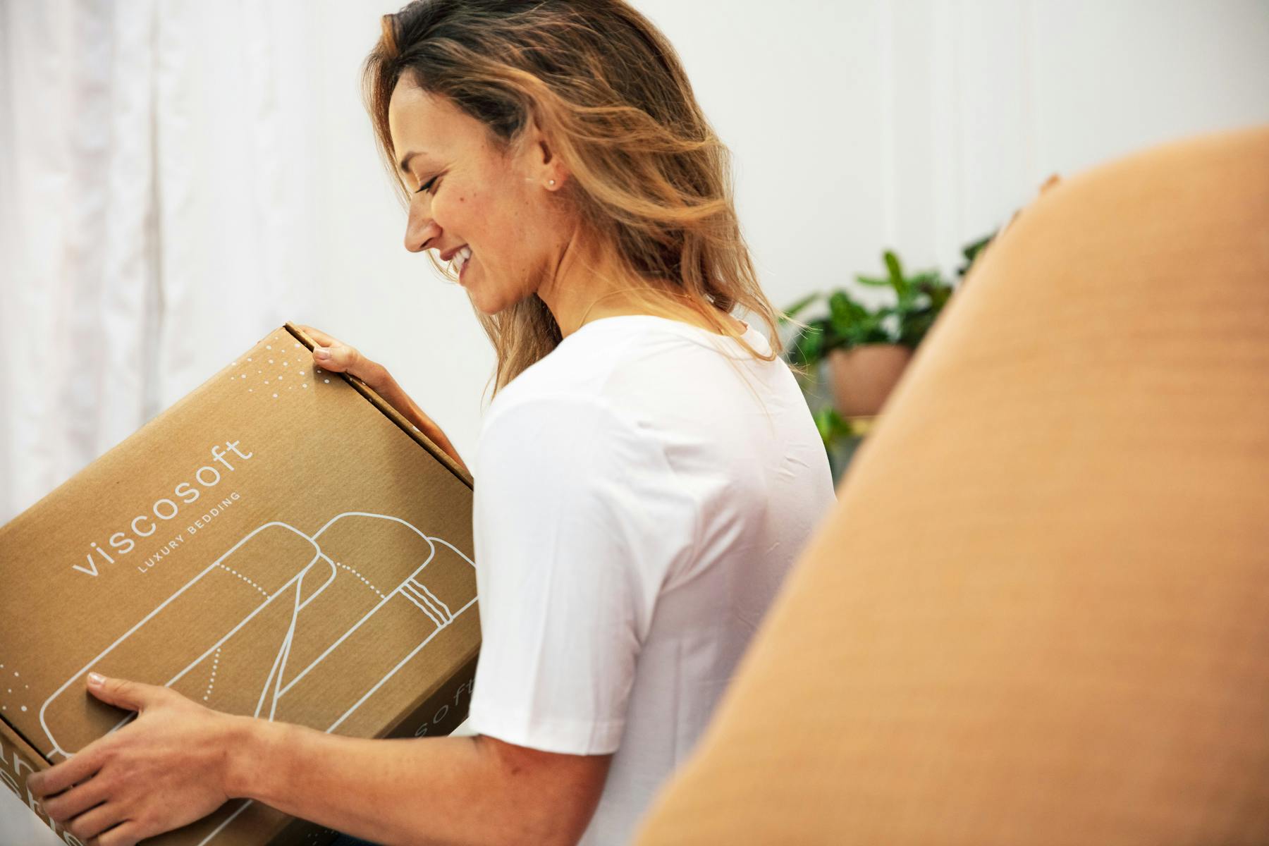 woman smiling while holding a box of organic cotton sheets