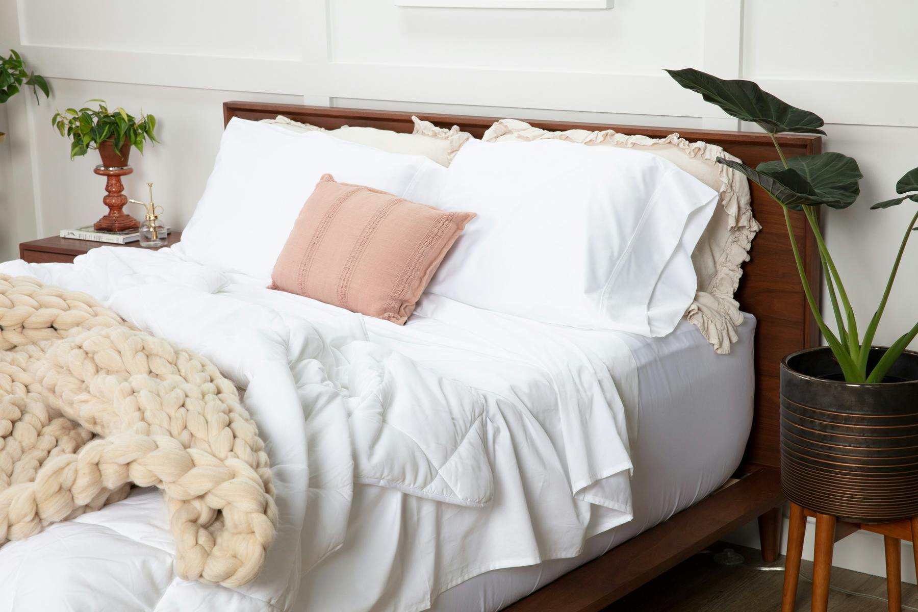 a bed made with white sheets and a white comforter with a beige throw blanket at the end of the bed and a pink throw pillow