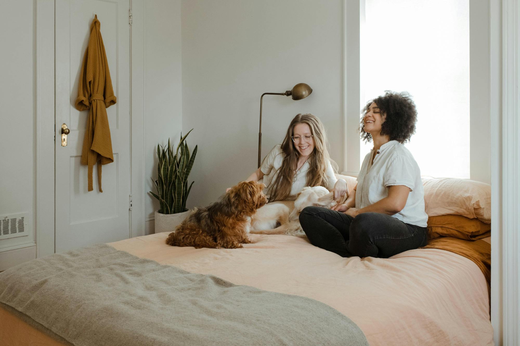 two women and their dog lounging and smiling on a bed