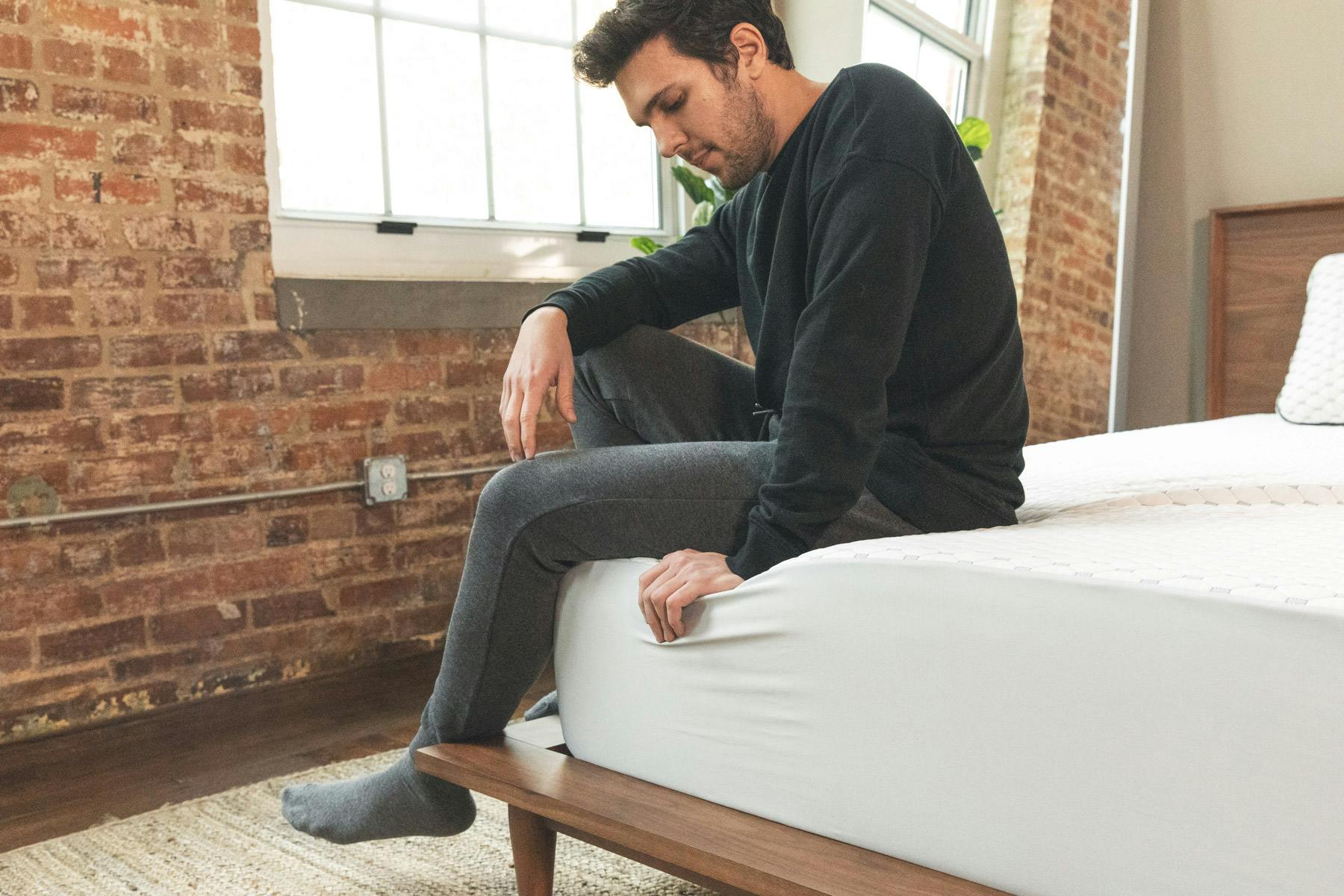 A man sitting on the corner of a bed that is fitted with a mattress protector