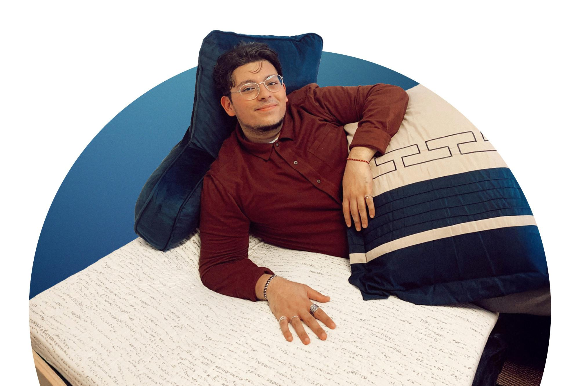 Man lounging on college dorm bed with textured mattress topper and large pillows.
