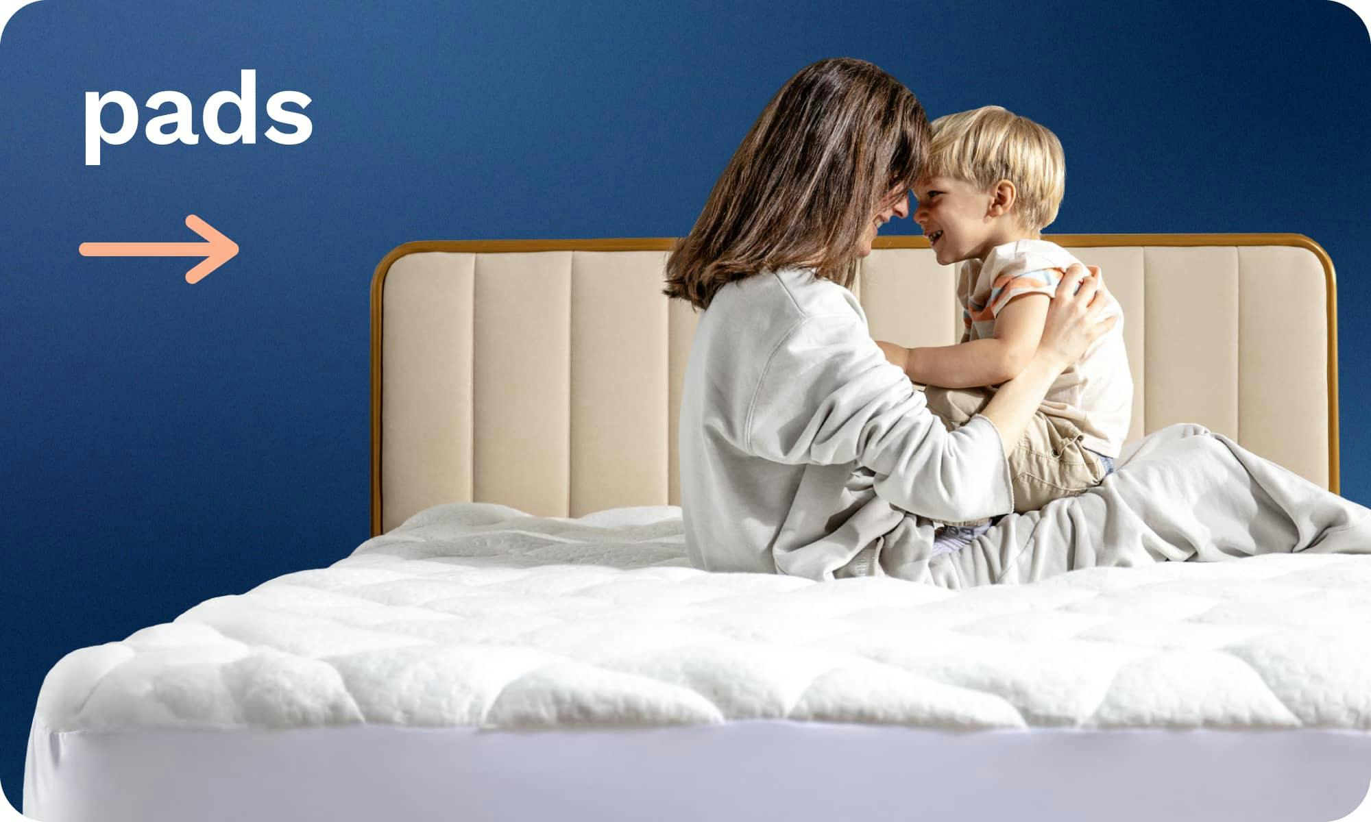 Mattress Pads; A brunette woman and her child smiling at each other while sitting on a quilted white mattress pad