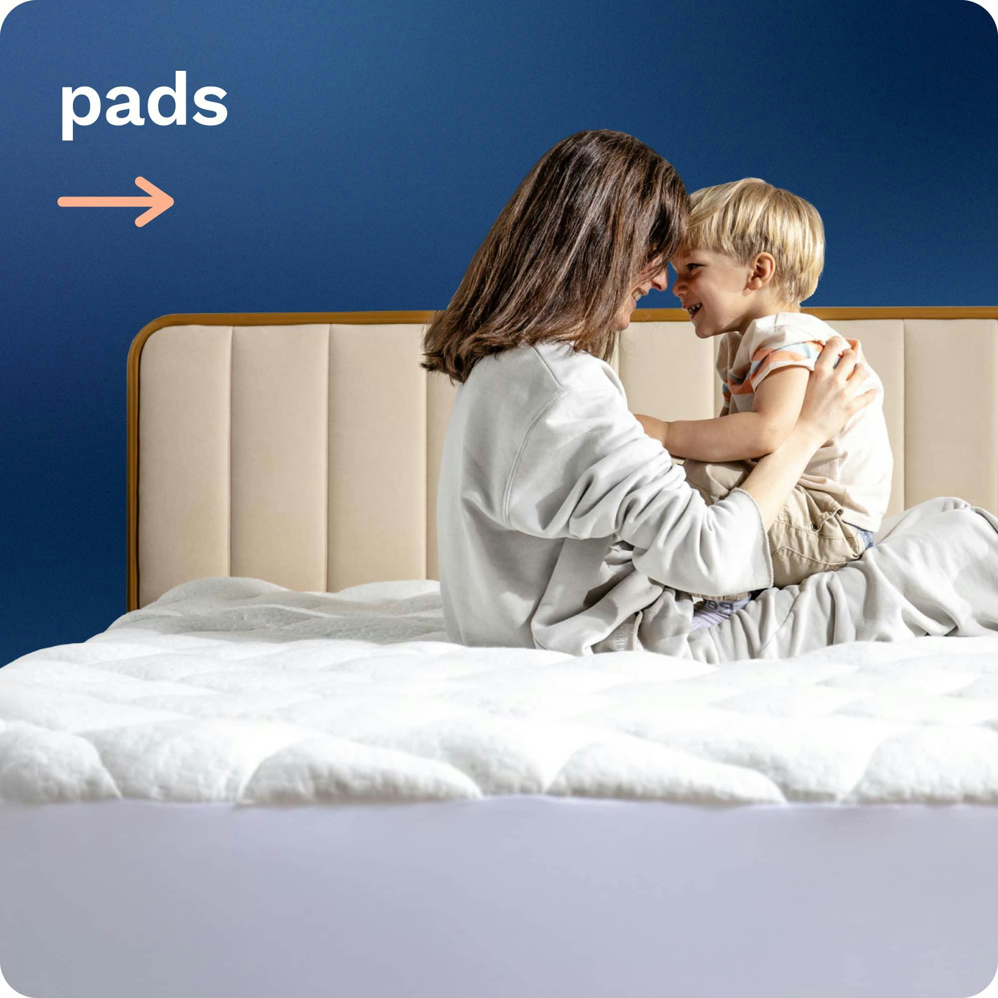 Mattress Pads; A brunette woman and her child smiling at each other while sitting on a quilted white mattress pad