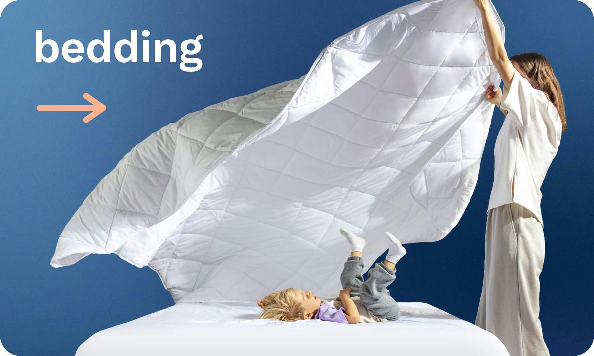 Bedding; A mom fluffing a quilted white comforter over her son who lays on the bed laughing
