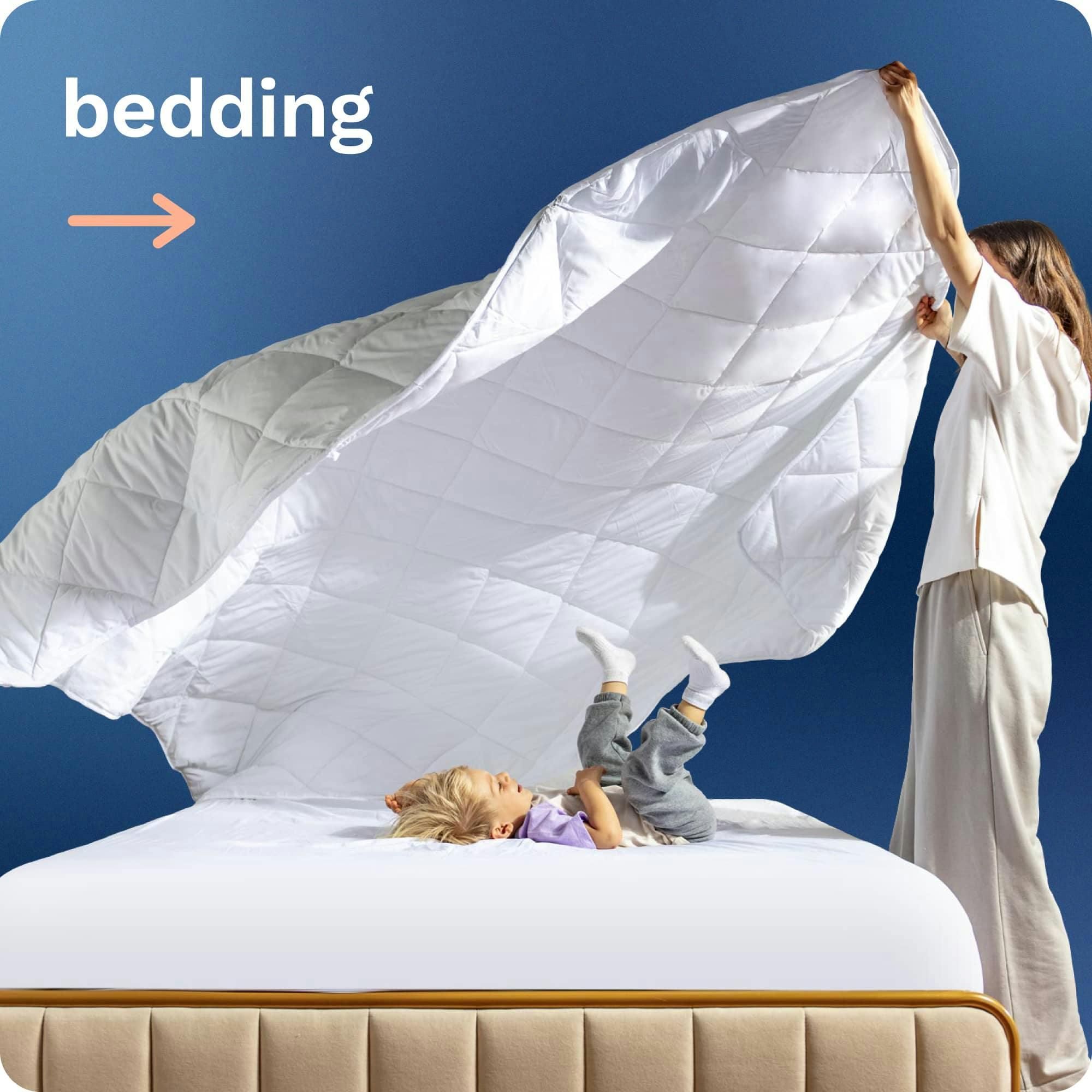 Bedding; A mom fluffing a quilted white comforter over her son who lays on the bed laughing
