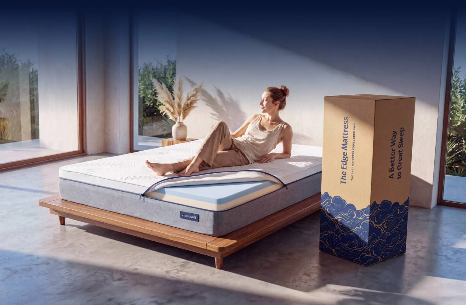 A woman lounging on a white and gray mattress with the corner unzipped and showing a dual memory foam comfort layer.
