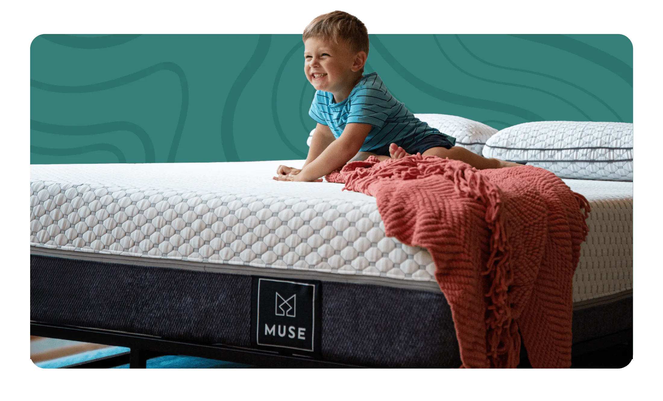 A kid smiling wide while sitting on a mattress with a gray bottom and white top