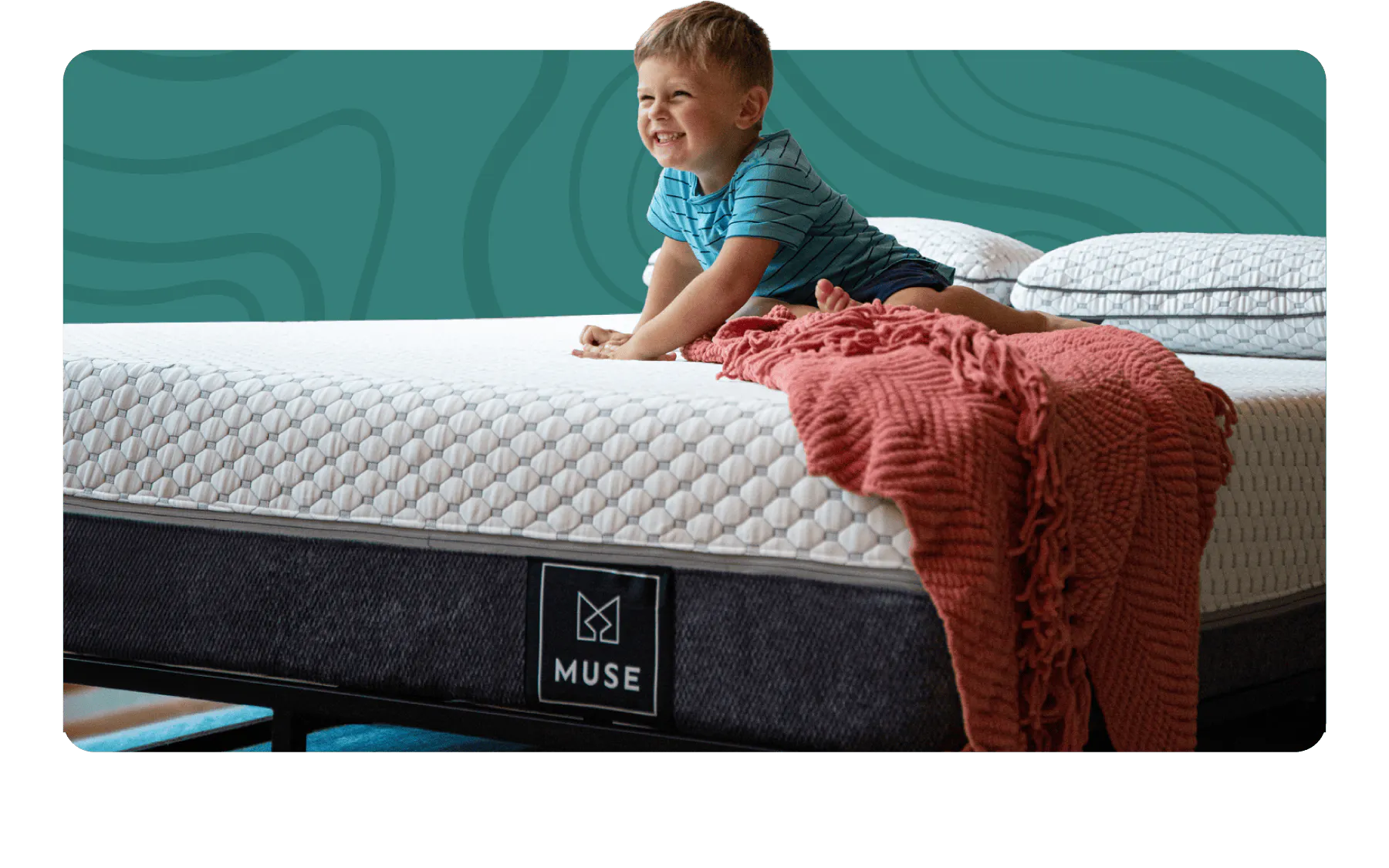 A kid smiling wide while sitting on a mattress with a gray bottom and white top