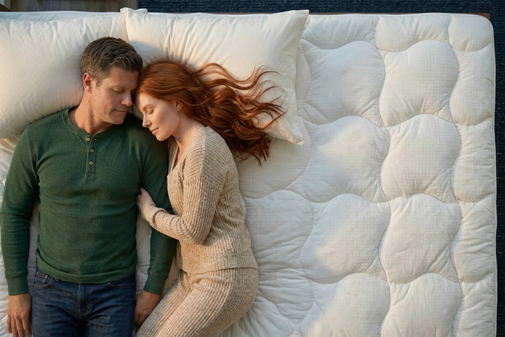 An aerial view of a man and woman cuddling on a quilted mattress pad