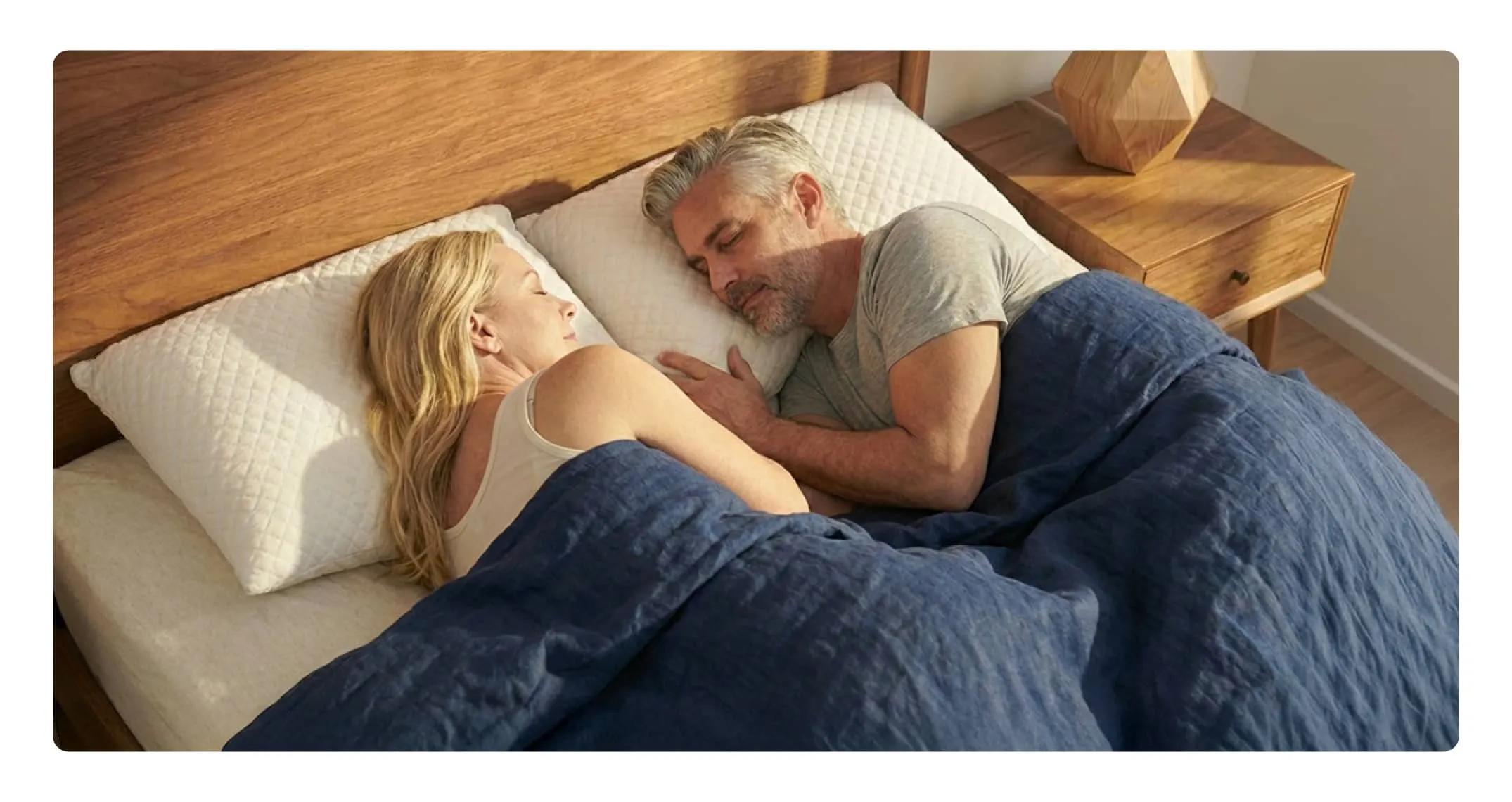 A man and woman sleeping peacefully in bed while using plush white pillows.